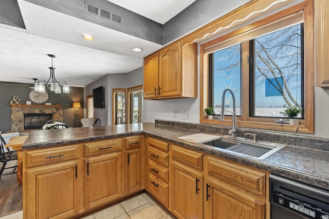 kitchen featuring dishwasher, a stone fireplace, sink, hanging light fixtures, and kitchen peninsula