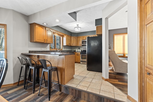 kitchen with light wood-type flooring, a textured ceiling, a kitchen bar, kitchen peninsula, and stainless steel appliances