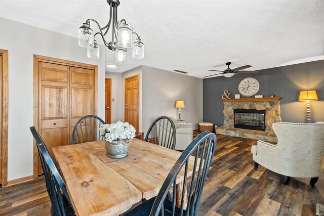 dining room featuring a textured ceiling, ceiling fan with notable chandelier, dark hardwood / wood-style flooring, and a fireplace