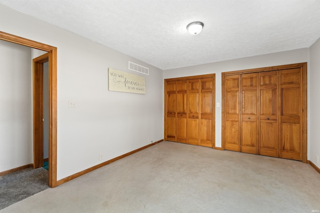 unfurnished bedroom with a textured ceiling, light carpet, and multiple closets