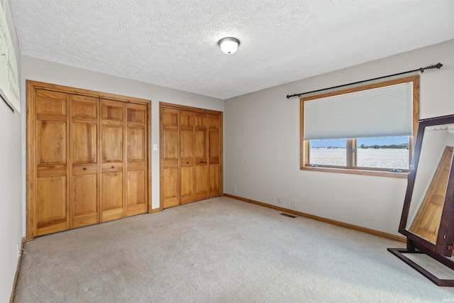 unfurnished bedroom with a textured ceiling, two closets, and light colored carpet