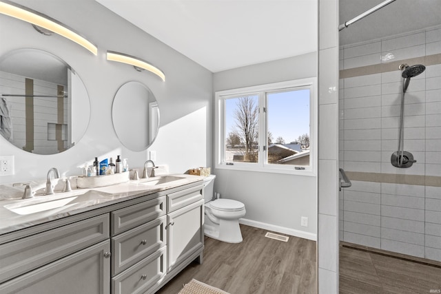 bathroom with tiled shower, hardwood / wood-style floors, vanity, and toilet