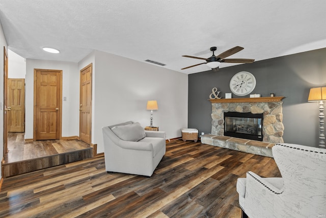 living room with a fireplace, ceiling fan, dark hardwood / wood-style flooring, and a textured ceiling