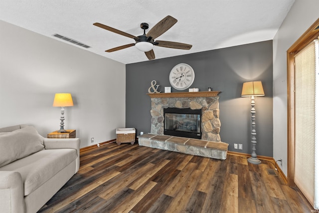 living room with a textured ceiling, a fireplace, ceiling fan, and dark wood-type flooring