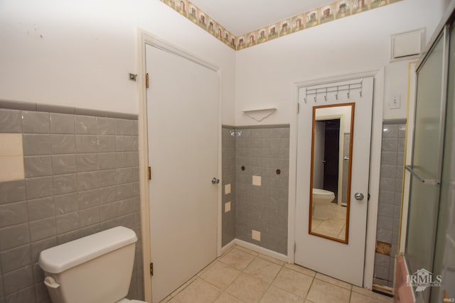 bathroom featuring tile patterned floors, a shower with shower door, tile walls, and toilet