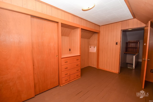 unfurnished bedroom featuring wood walls, a closet, wood-type flooring, and lofted ceiling