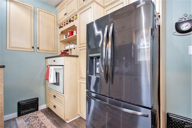 kitchen featuring cream cabinetry, oven, stainless steel fridge, and dark wood-type flooring