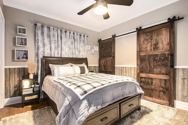 bedroom with wood walls, ceiling fan, a barn door, ornamental molding, and wood-type flooring