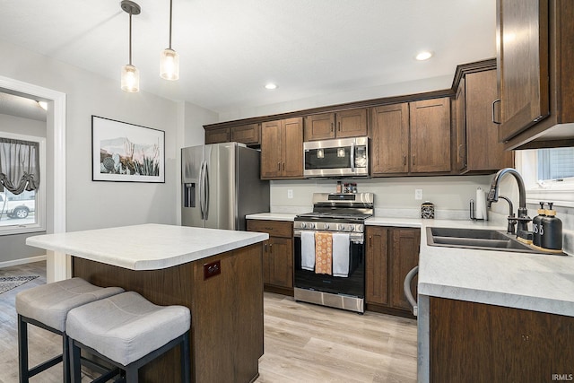 kitchen featuring pendant lighting, a center island, sink, light wood-type flooring, and stainless steel appliances