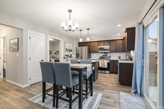 dining space featuring sink, an inviting chandelier, a textured ceiling, and light wood-type flooring