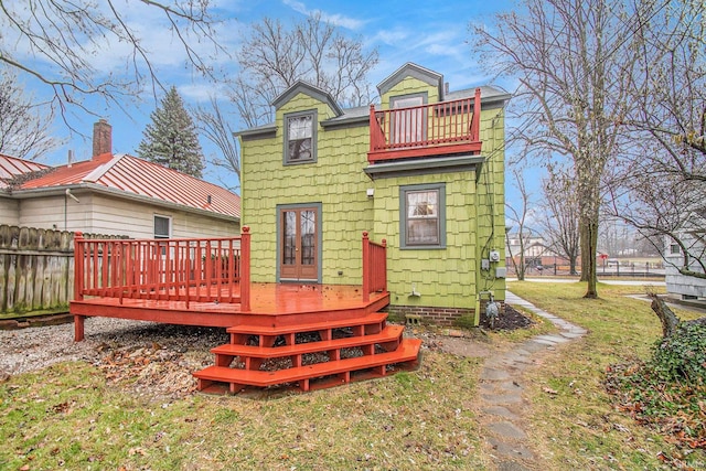 rear view of property featuring a balcony, a yard, and a deck