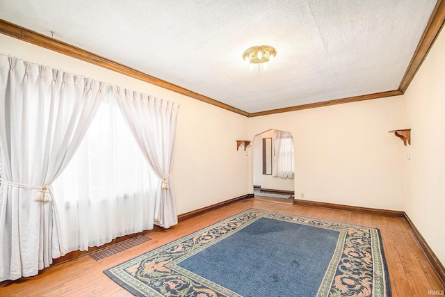 spare room featuring crown molding, wood-type flooring, and a textured ceiling