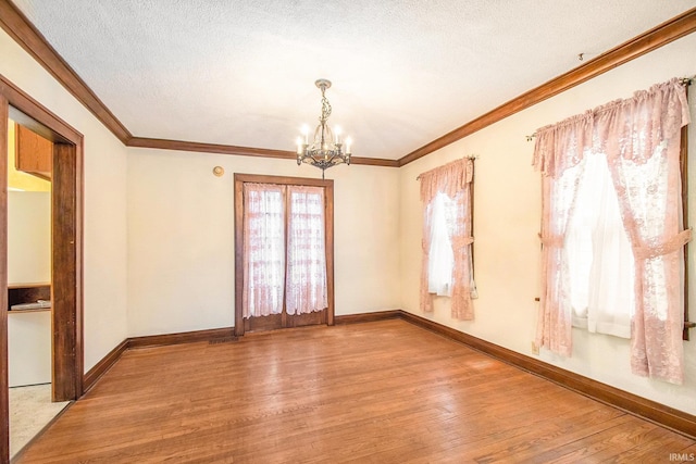 spare room with a textured ceiling, an inviting chandelier, light hardwood / wood-style flooring, and ornamental molding