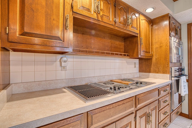 kitchen featuring backsplash, light tile patterned floors, stainless steel appliances, and a textured ceiling