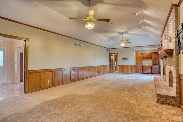 unfurnished living room with a textured ceiling, light colored carpet, ornamental molding, and a fireplace