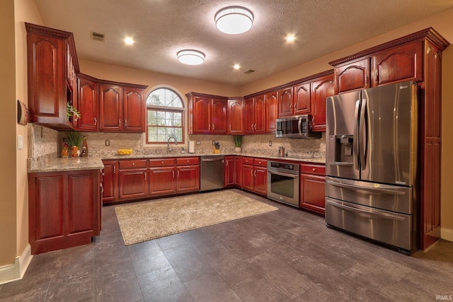 kitchen featuring backsplash, light stone counters, a textured ceiling, stainless steel appliances, and sink