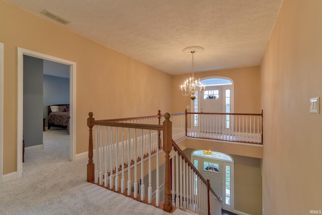 staircase with carpet flooring, a textured ceiling, and a notable chandelier