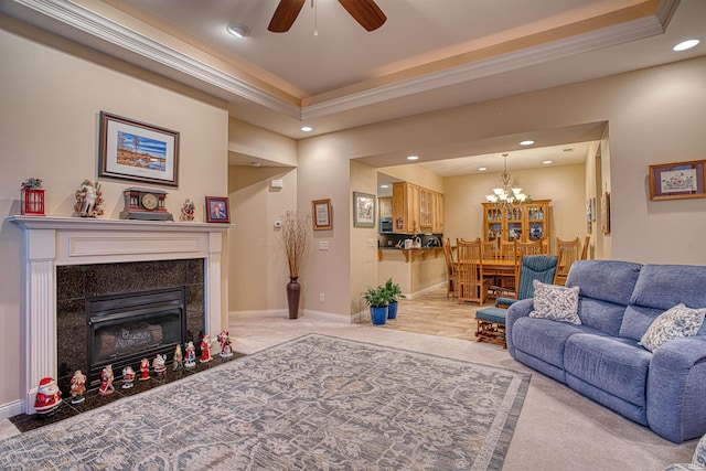 carpeted living room with a tray ceiling, a tile fireplace, crown molding, and ceiling fan with notable chandelier