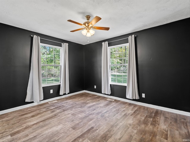 empty room with wood-type flooring, a textured ceiling, a wealth of natural light, and ceiling fan