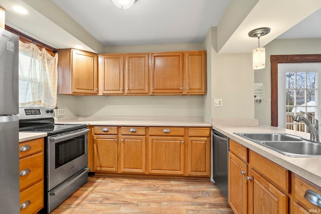 kitchen featuring sink, light wood-type flooring, hanging light fixtures, and appliances with stainless steel finishes