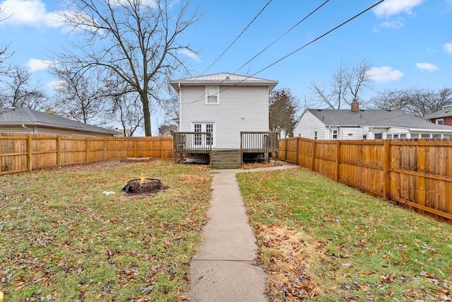 rear view of house with a wooden deck, a yard, and a fire pit