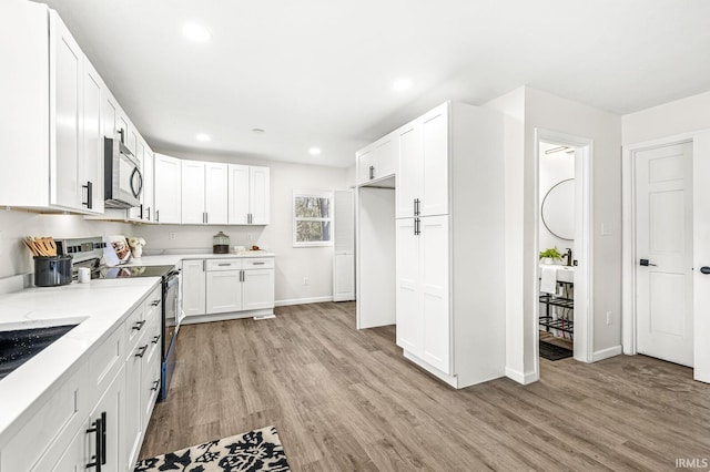 kitchen featuring light stone countertops, light wood-type flooring, white cabinetry, and appliances with stainless steel finishes