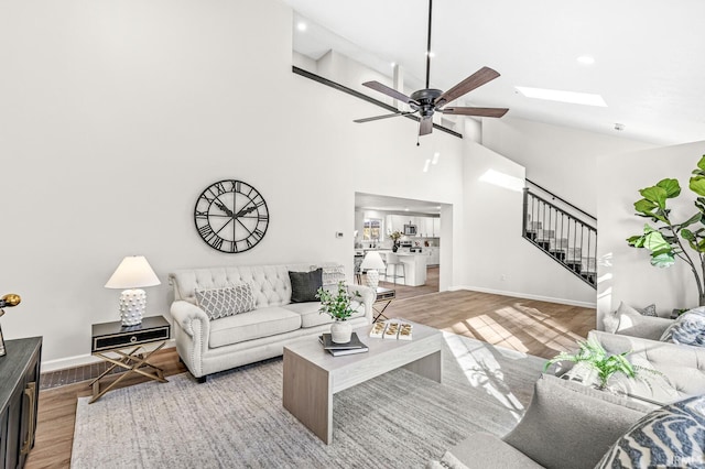 living room with a skylight, ceiling fan, high vaulted ceiling, and light hardwood / wood-style floors