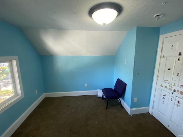 unfurnished room with a textured ceiling, lofted ceiling, and dark colored carpet