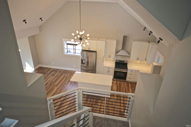 kitchen featuring appliances with stainless steel finishes, wall chimney exhaust hood, high vaulted ceiling, white cabinets, and a chandelier