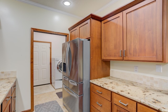 kitchen with stainless steel refrigerator with ice dispenser, light stone counters, crown molding, washer / clothes dryer, and light tile patterned flooring