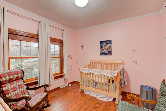 bedroom featuring a crib, hardwood / wood-style floors, a textured ceiling, and ornamental molding