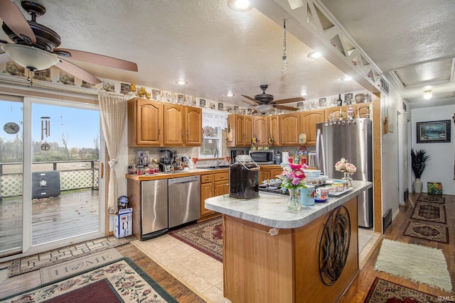 kitchen with ceiling fan, a kitchen island, a textured ceiling, light tile patterned floors, and appliances with stainless steel finishes