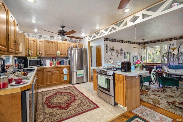 kitchen with sink, a center island, a textured ceiling, light tile patterned floors, and appliances with stainless steel finishes