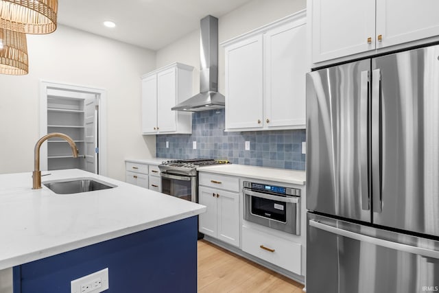 kitchen with appliances with stainless steel finishes, sink, wall chimney range hood, light hardwood / wood-style flooring, and white cabinets