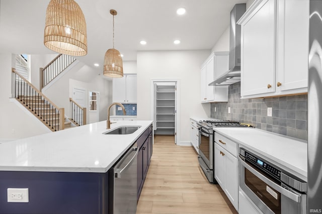 kitchen featuring a center island with sink, sink, hanging light fixtures, wall chimney exhaust hood, and stainless steel appliances