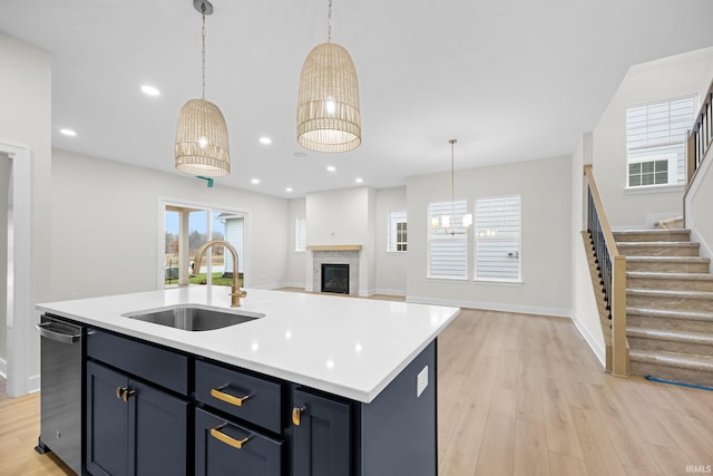 kitchen with sink, decorative light fixtures, light hardwood / wood-style flooring, dishwasher, and an island with sink