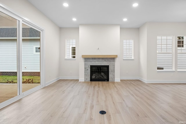 unfurnished living room with a tile fireplace, a wealth of natural light, and light wood-type flooring