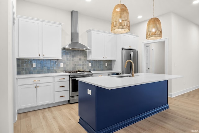 kitchen with white cabinets, hanging light fixtures, wall chimney exhaust hood, appliances with stainless steel finishes, and light hardwood / wood-style floors