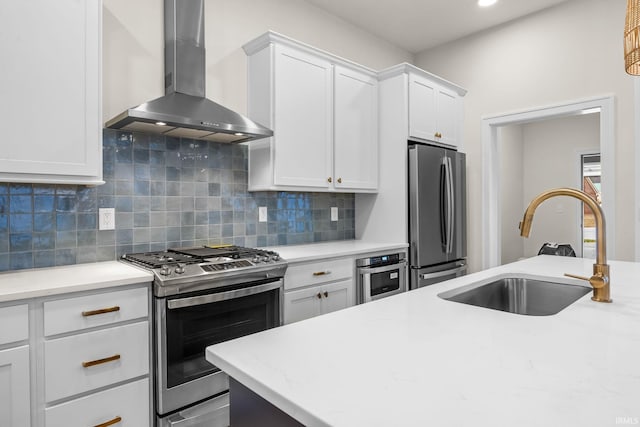 kitchen with decorative backsplash, appliances with stainless steel finishes, sink, wall chimney range hood, and white cabinetry