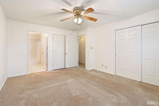 unfurnished bedroom featuring ensuite bath, ceiling fan, multiple closets, a textured ceiling, and light carpet