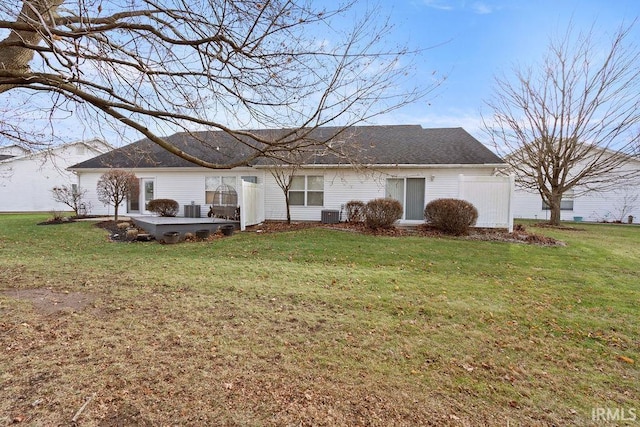 rear view of property featuring central air condition unit and a lawn