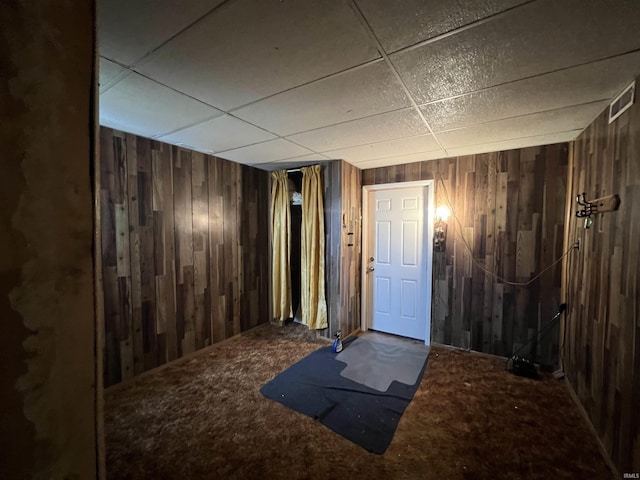 interior space with carpet flooring, a drop ceiling, and wood walls