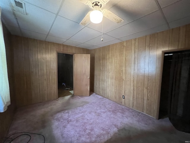 carpeted spare room featuring wooden walls, a drop ceiling, and ceiling fan