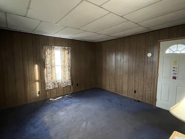 empty room with a drop ceiling, a wealth of natural light, and wood walls