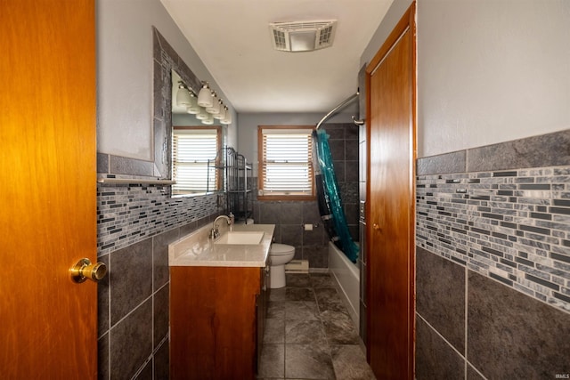 full bathroom with shower / tub combo, tile patterned flooring, toilet, vanity, and tile walls