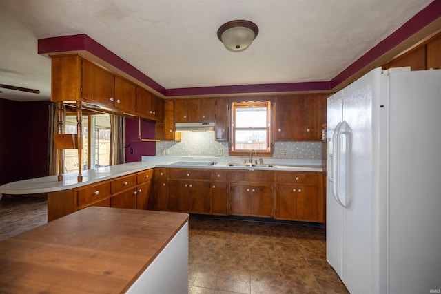 kitchen featuring ceiling fan, sink, white refrigerator with ice dispenser, backsplash, and kitchen peninsula