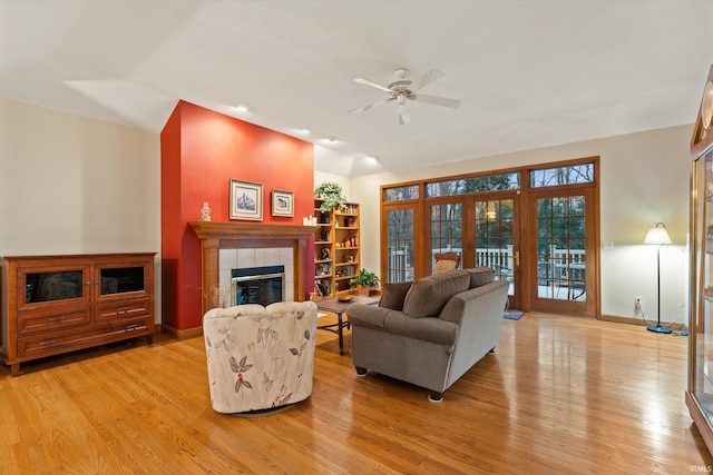 living room with french doors, vaulted ceiling, ceiling fan, light hardwood / wood-style flooring, and a tiled fireplace