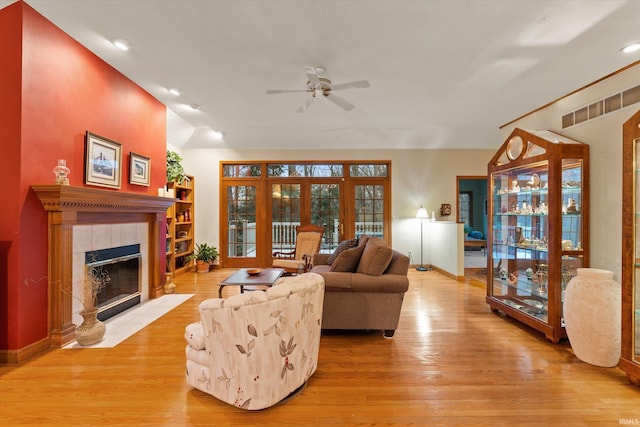 living room featuring ceiling fan, light wood-type flooring, a tile fireplace, and vaulted ceiling