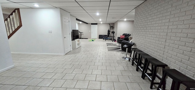 interior space featuring light tile patterned floors, a drop ceiling, and brick wall