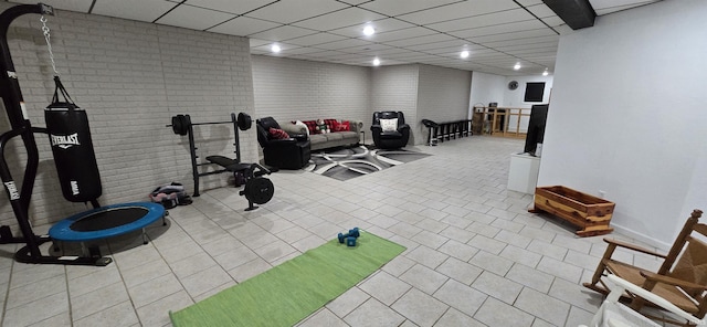 exercise area with a drop ceiling, light tile patterned floors, and brick wall